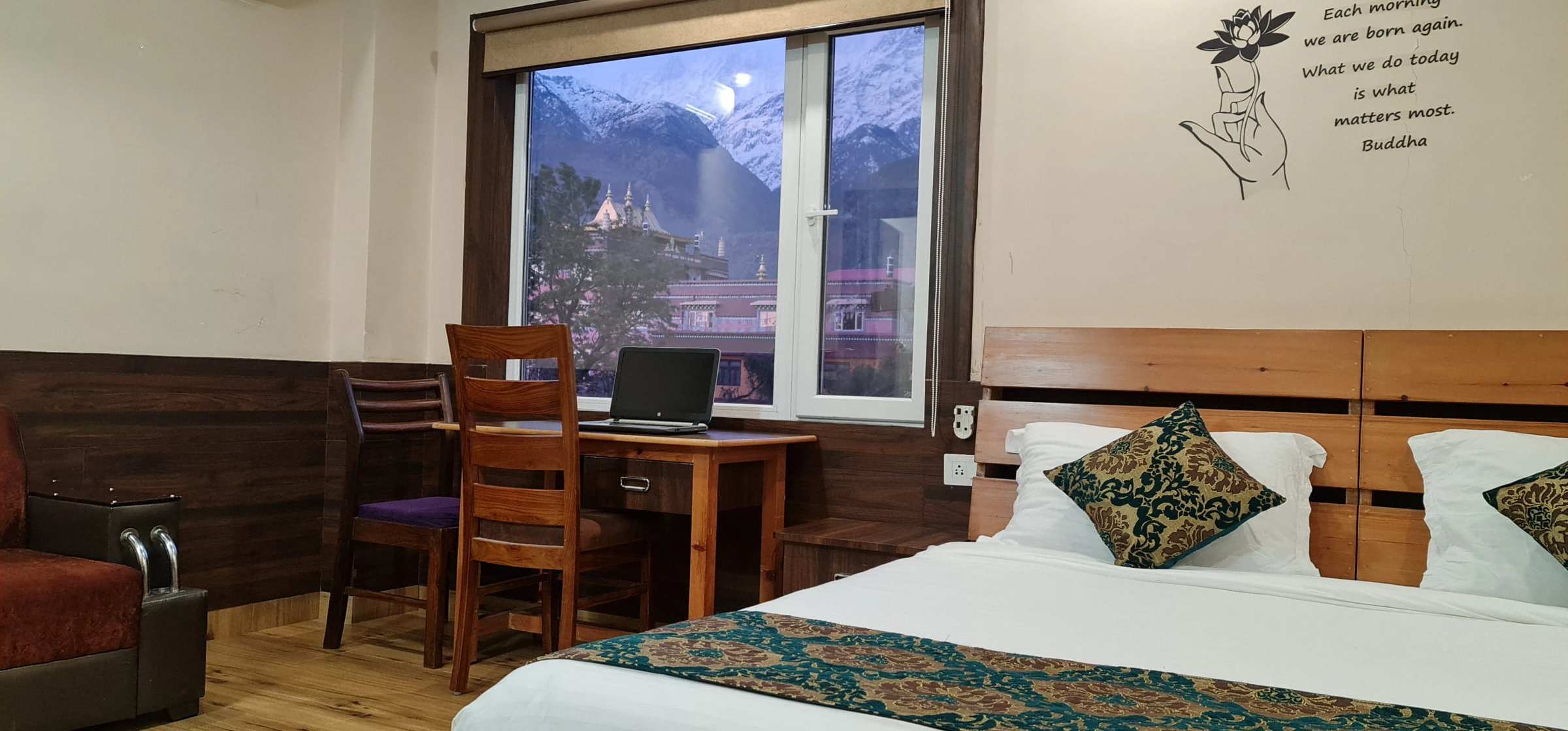 A Buddha House room whose window frames a monastery roof and the snow-capped Dhauladhar